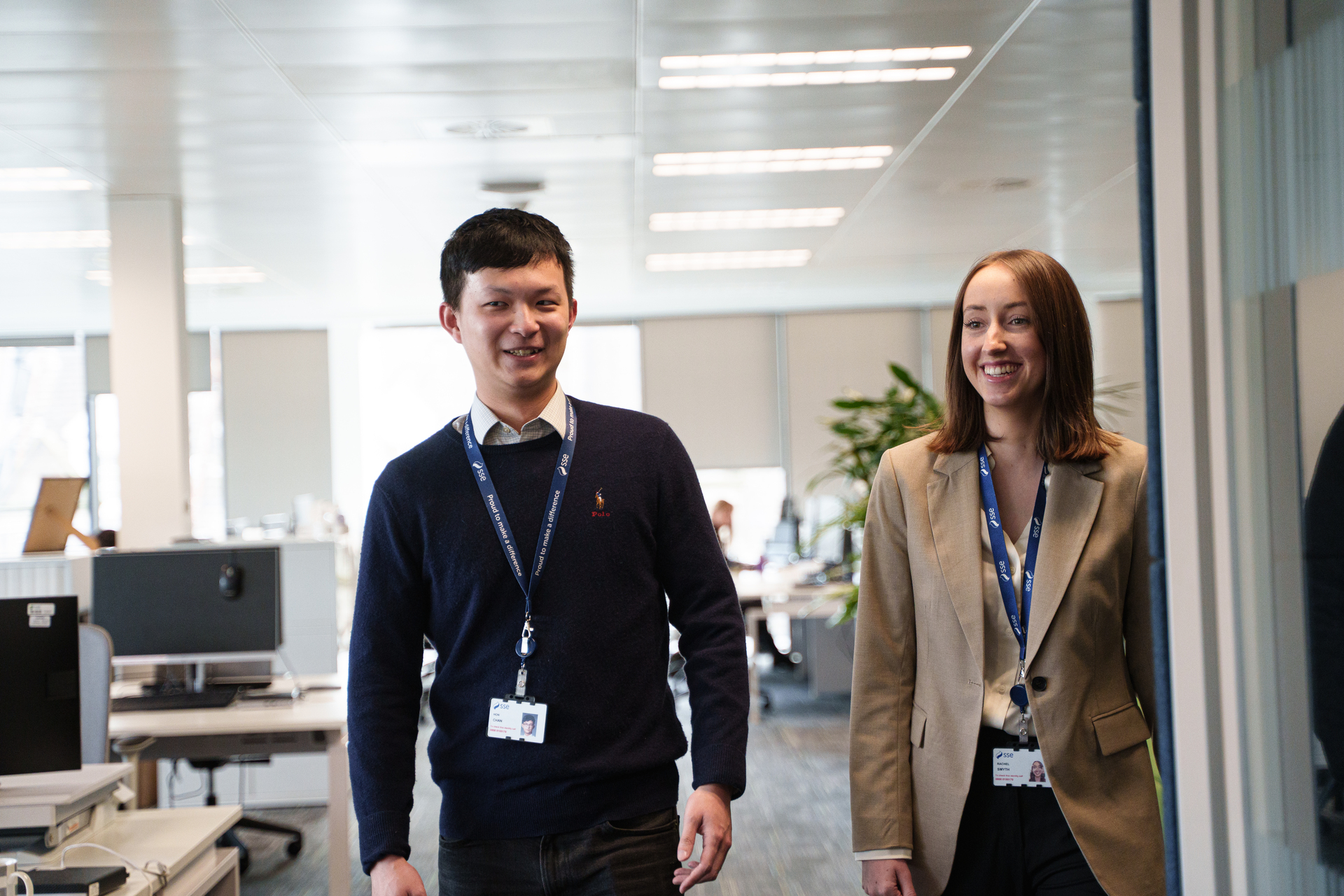 A male and female SSE colleague walking through an office smiling and dressed smartly