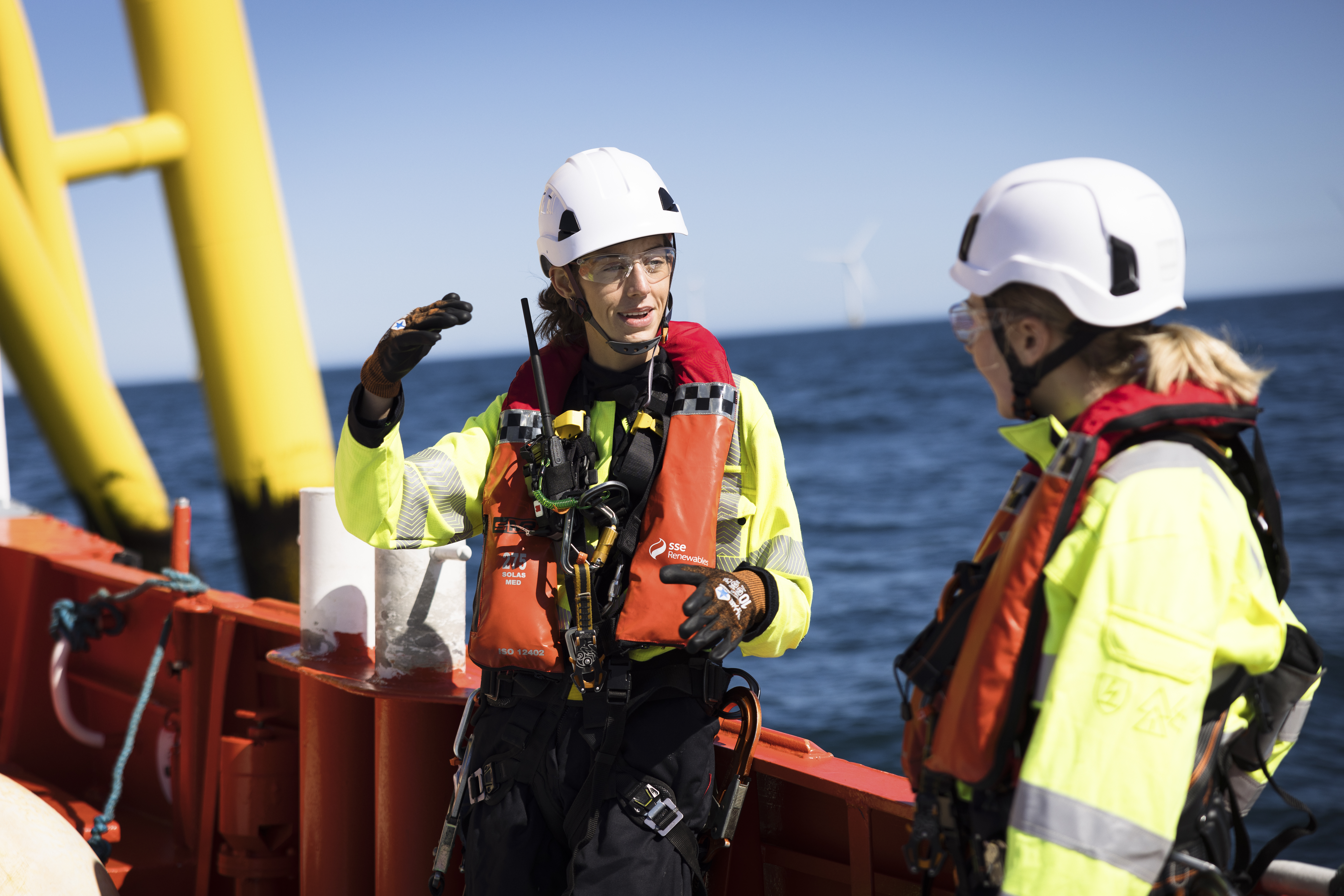 Two female engineers in PPE having a discussion on a boat at the bottom of an offshore wind turbine