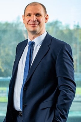Martin Pibworth standing smiling in a portrait photograph wearing a navy suit with a blue tie