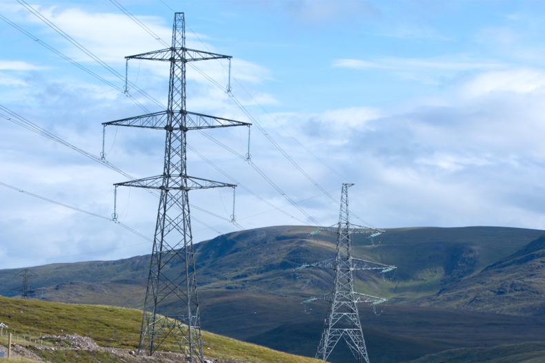 Electricity transmission towers carrying overhead power lines across Highland landscape in Scotland.