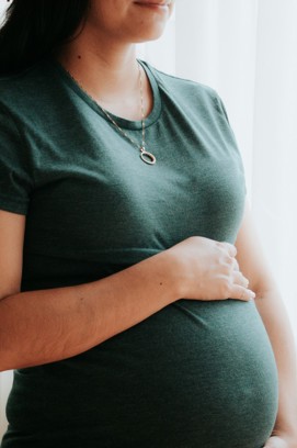 A woman standing in a green short sleeved top with her right hand resting on a large visible pregnancy bump 