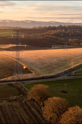Two transmission towers/pylons in a field surrounded by trees at sunset
