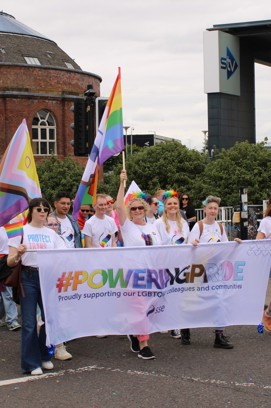 SSE colleagues taking part in a Pride march holding a banner that has #PoweringPride written on it in rainbow colours